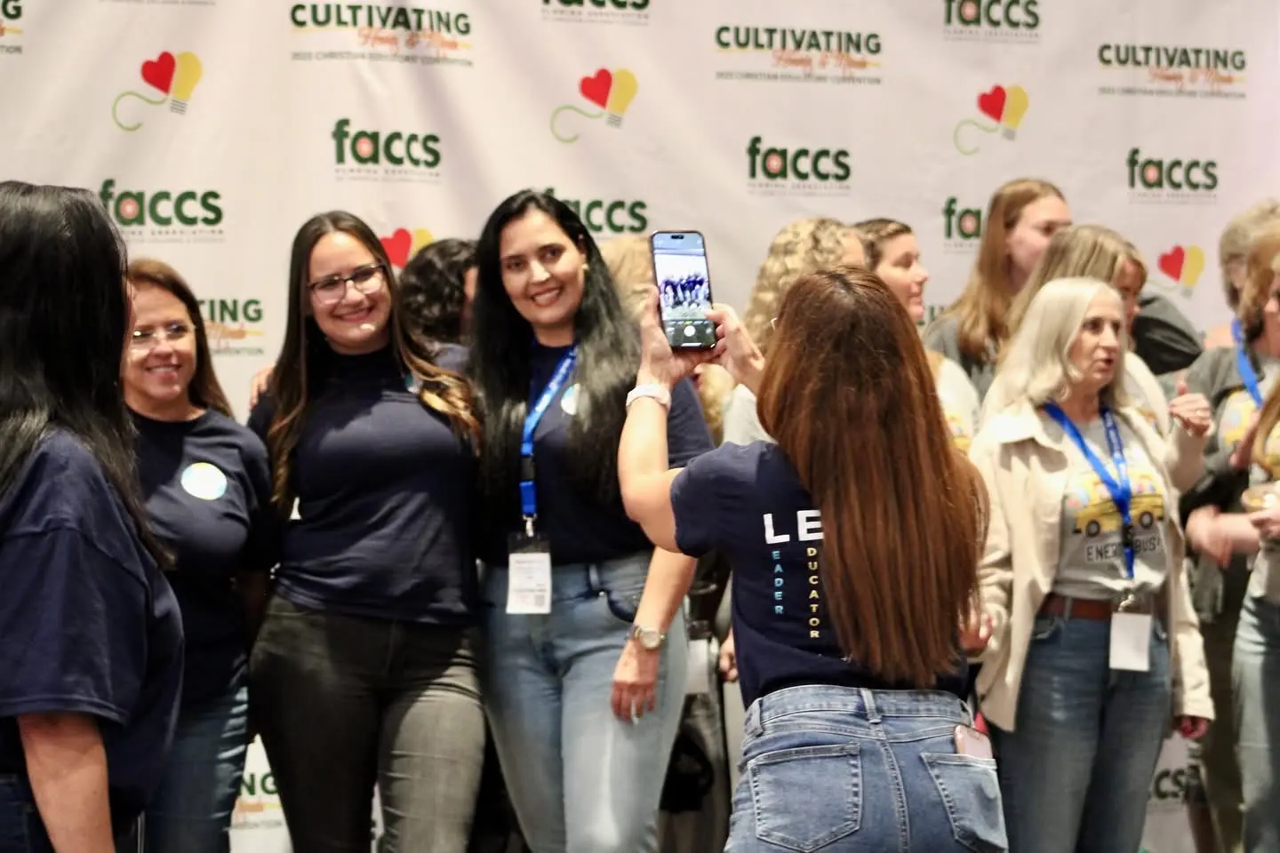 Convention attendees posing together in front of the FACCS backdrop while one of them takes a photo.