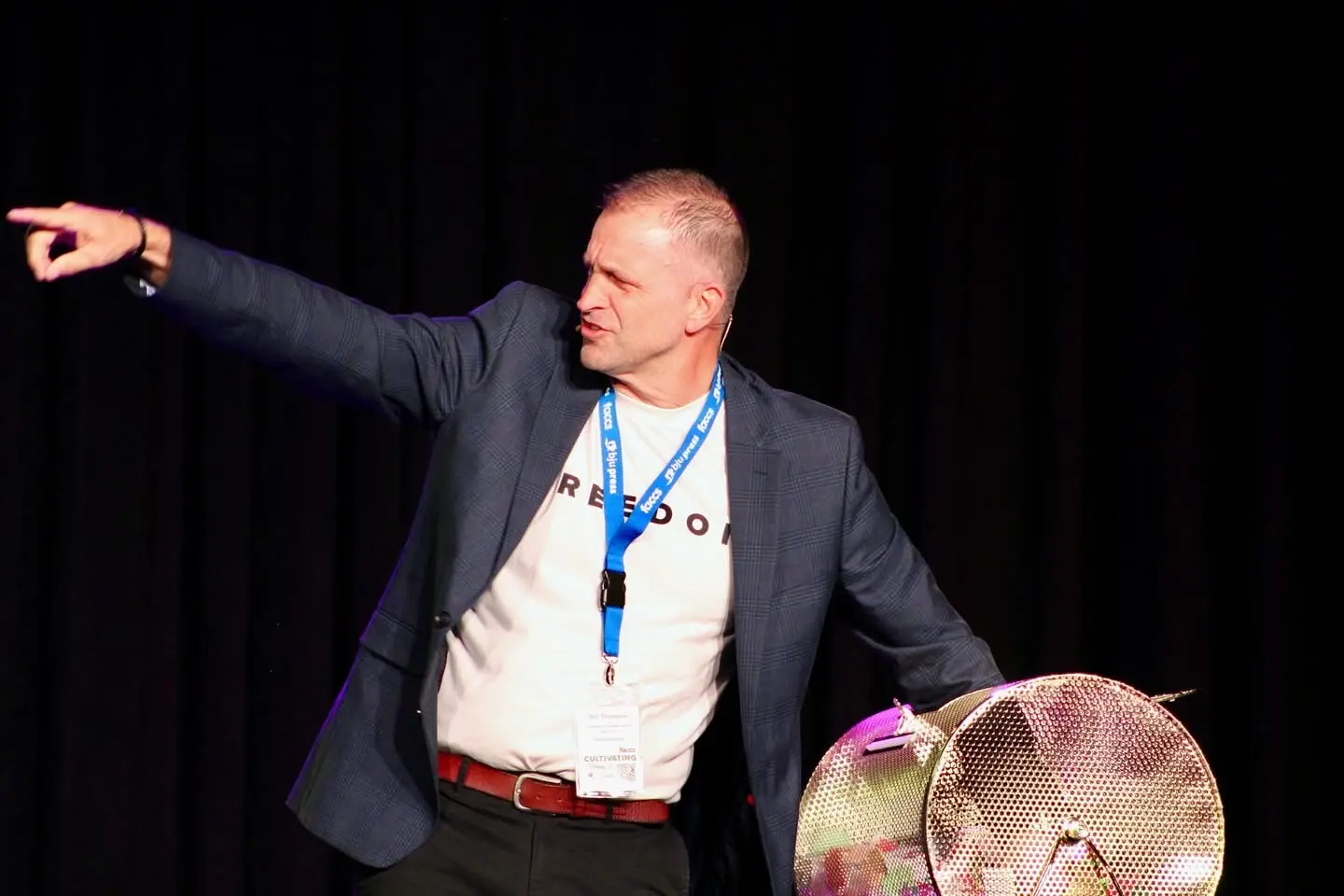 A speaker addressing the Educators' Convention from the main stage, arm outstretched mid-point.