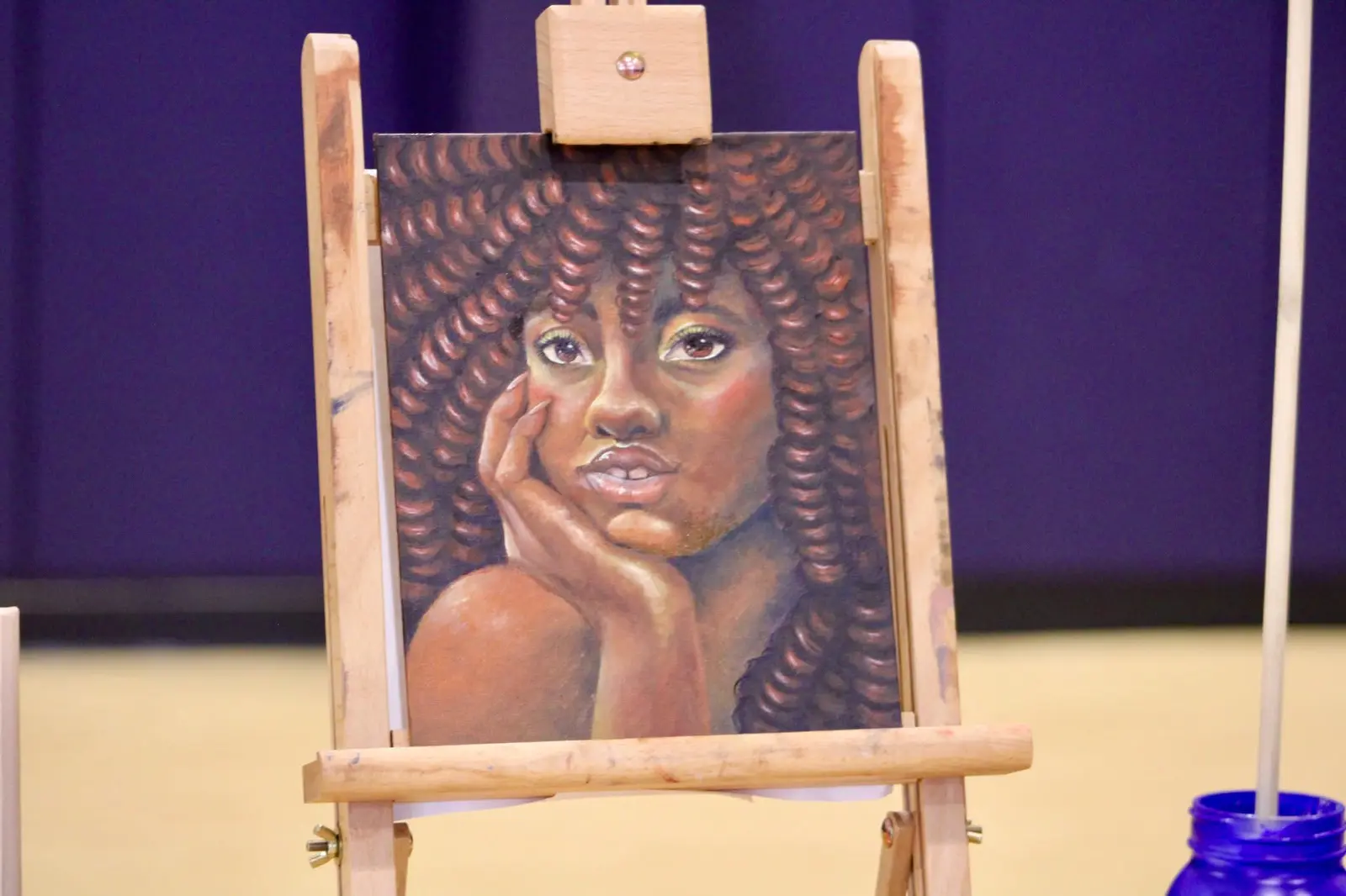 A student portrait painting displayed on a wooden easel at the art exhibition.
