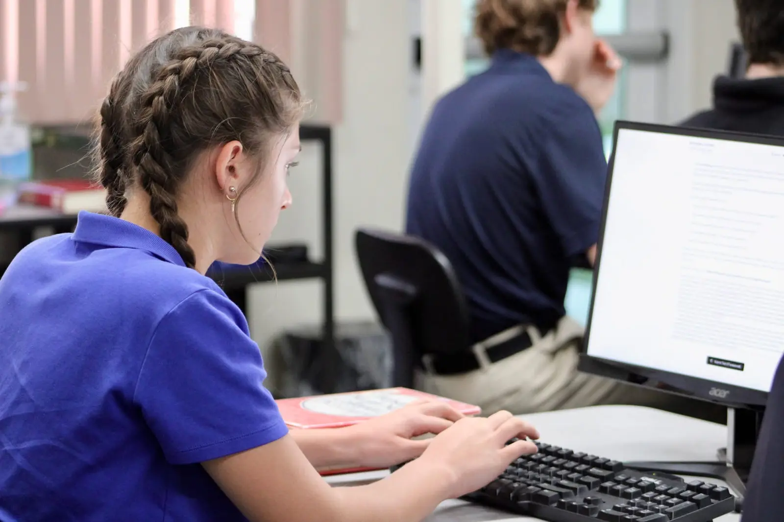 A high-school student typing at a keyboard during the keyboarding competition, a second competitor working behind her.