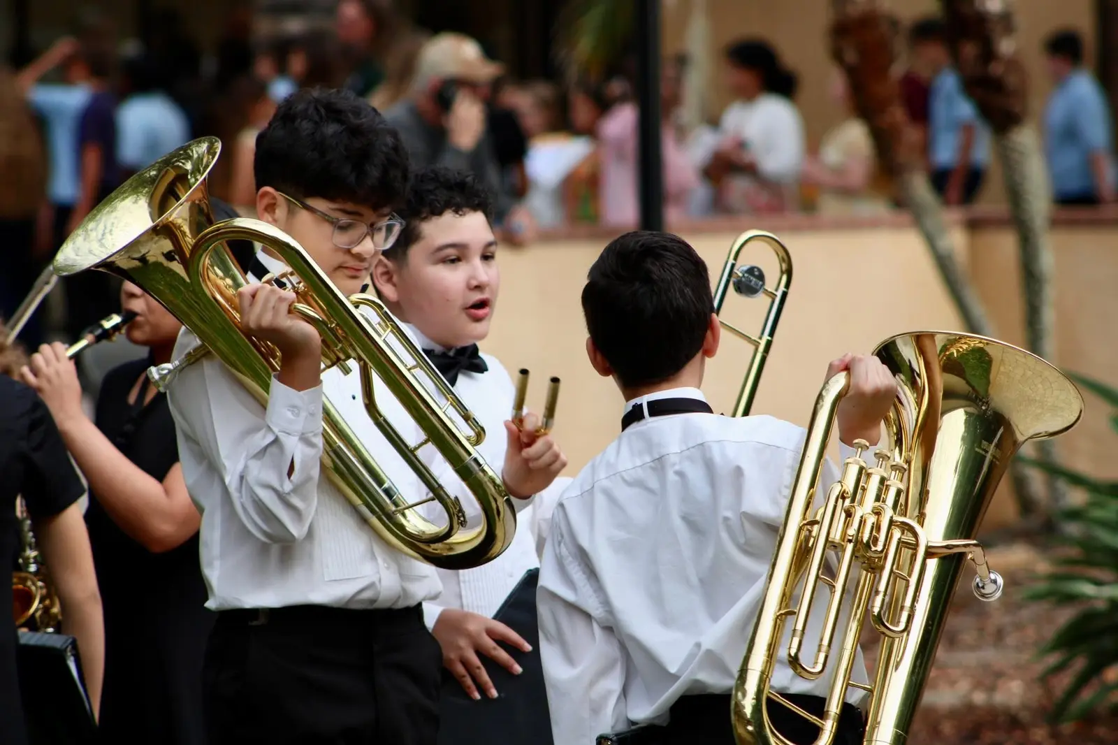 Three middle-school students in concert dress warming up on euphonium and trombone outside the competition venue.
