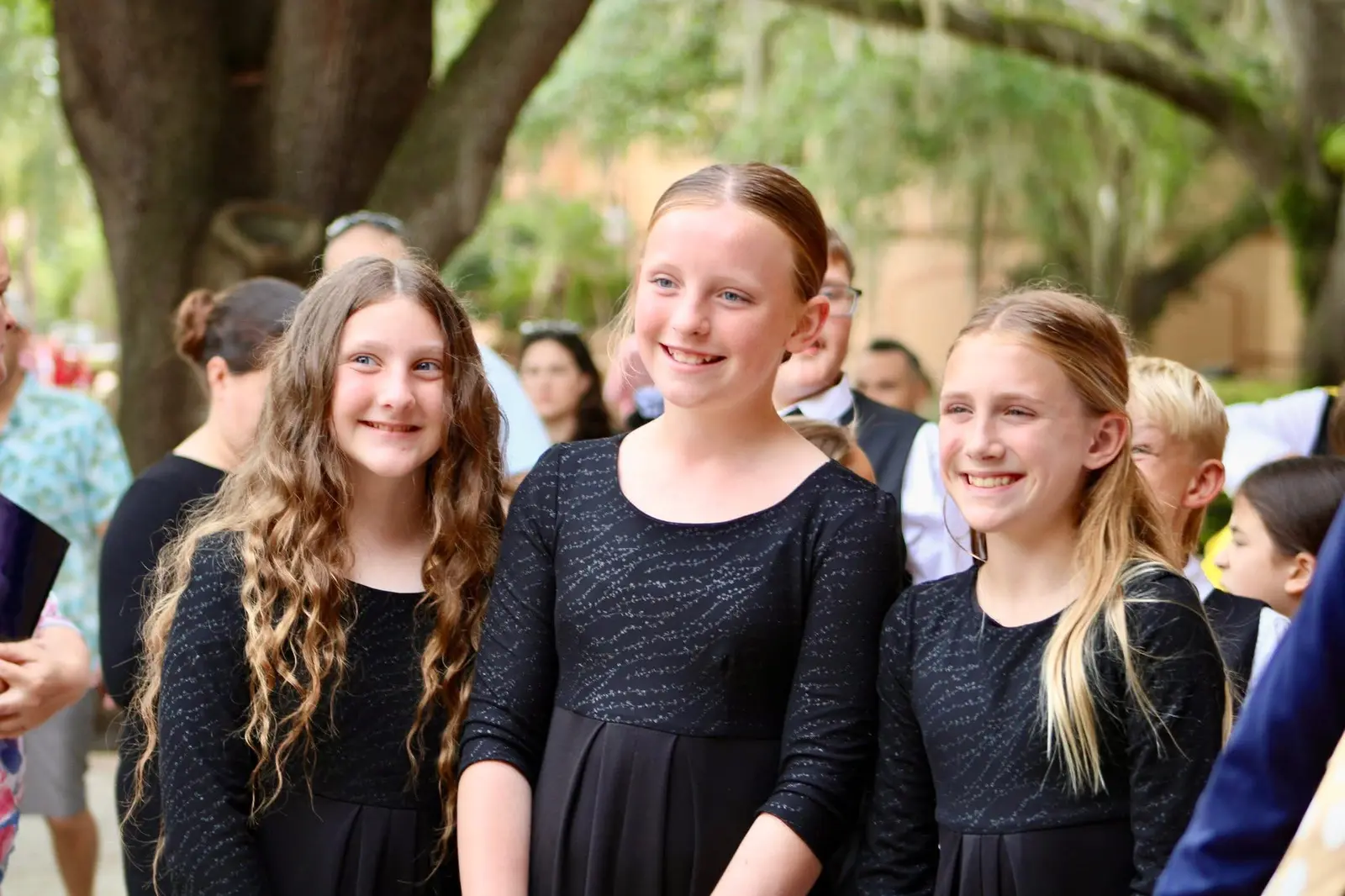 Three students in black performance dress smiling together outdoors between events.