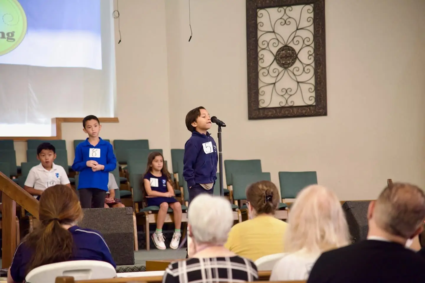 A young speller at the microphone while the other competitors wait in the rows behind.